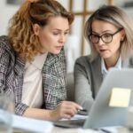 two women going over notes and looking at a laptop